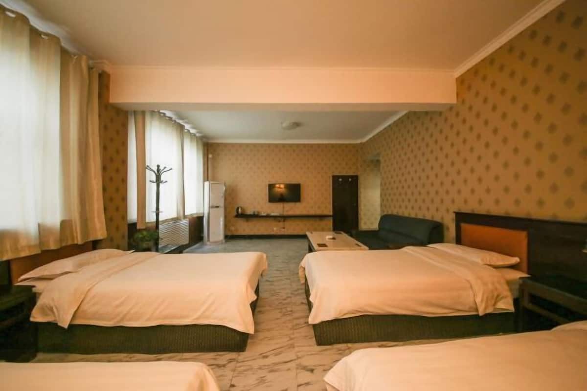 Ein Hotelzimmer mit zwei Einzelbetten, einem Fernseher, einem Schreibtisch und einem Stuhl.