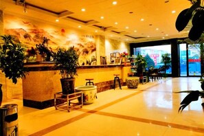 A hotel lobby with a reception desk, seating area, and large windows.