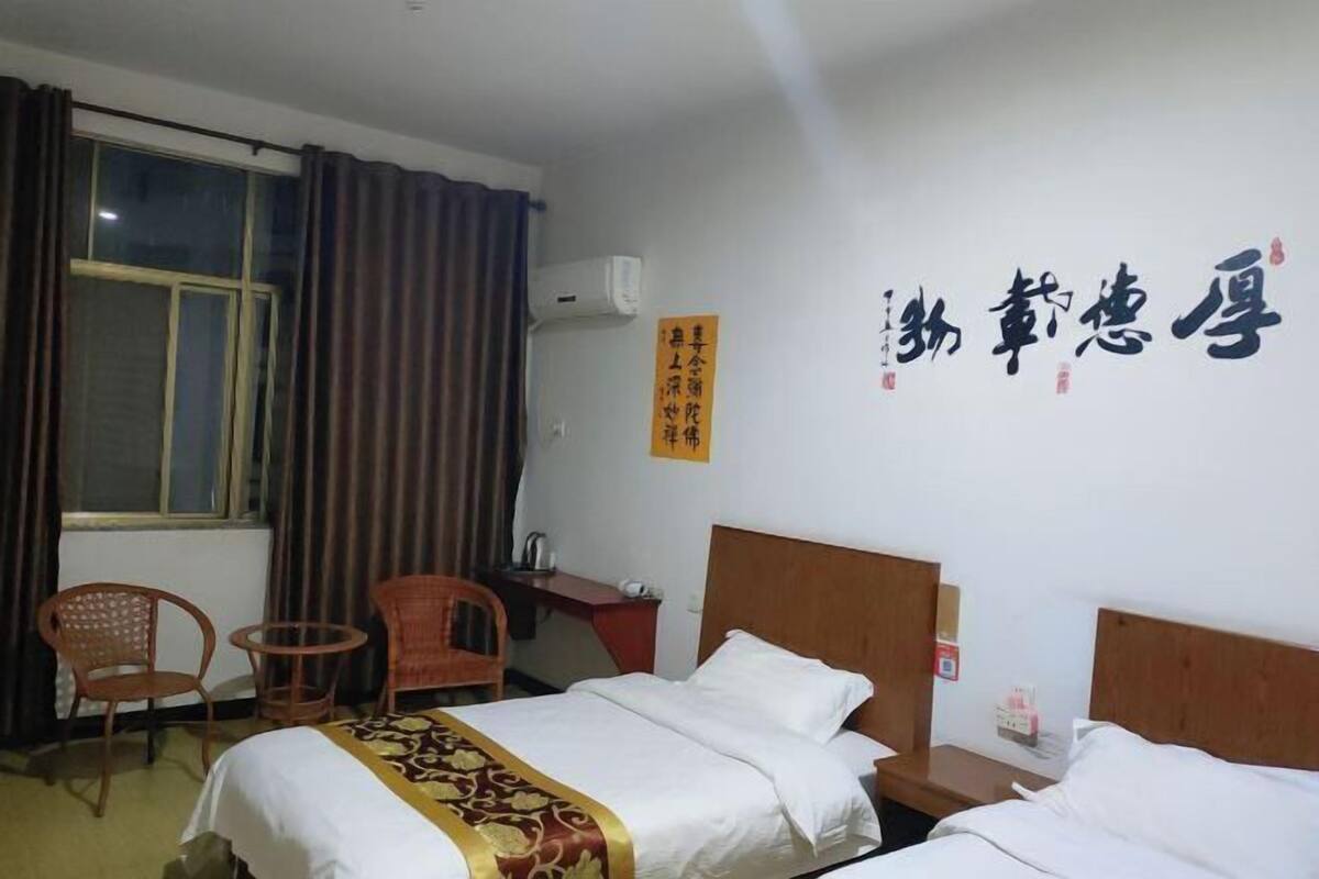 A hotel room with a bed, two chairs, a desk, and a window with curtains.