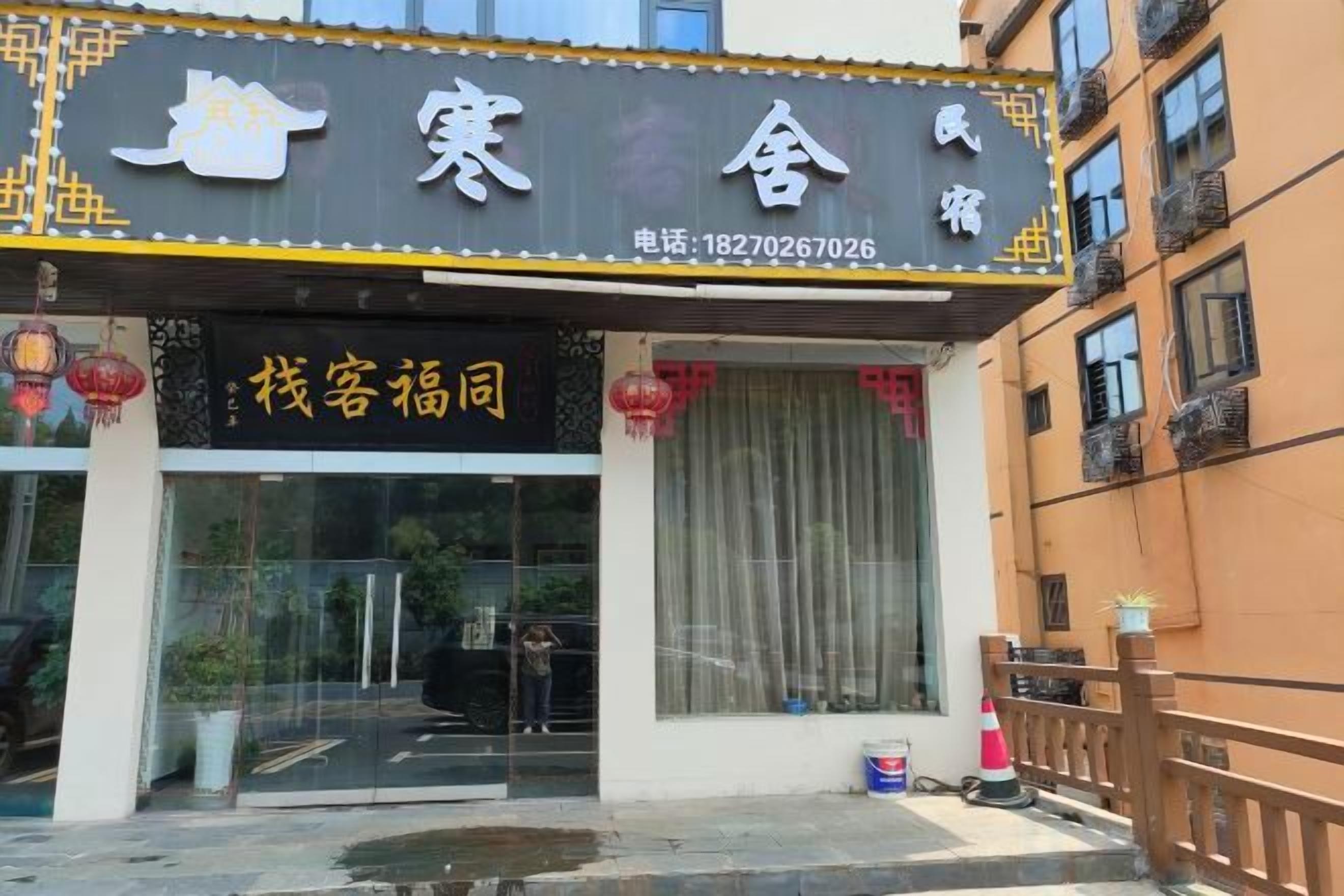 Entrada de un hotel con puerta de cristal, un número de teléfono y un letrero con caracteres chinos.