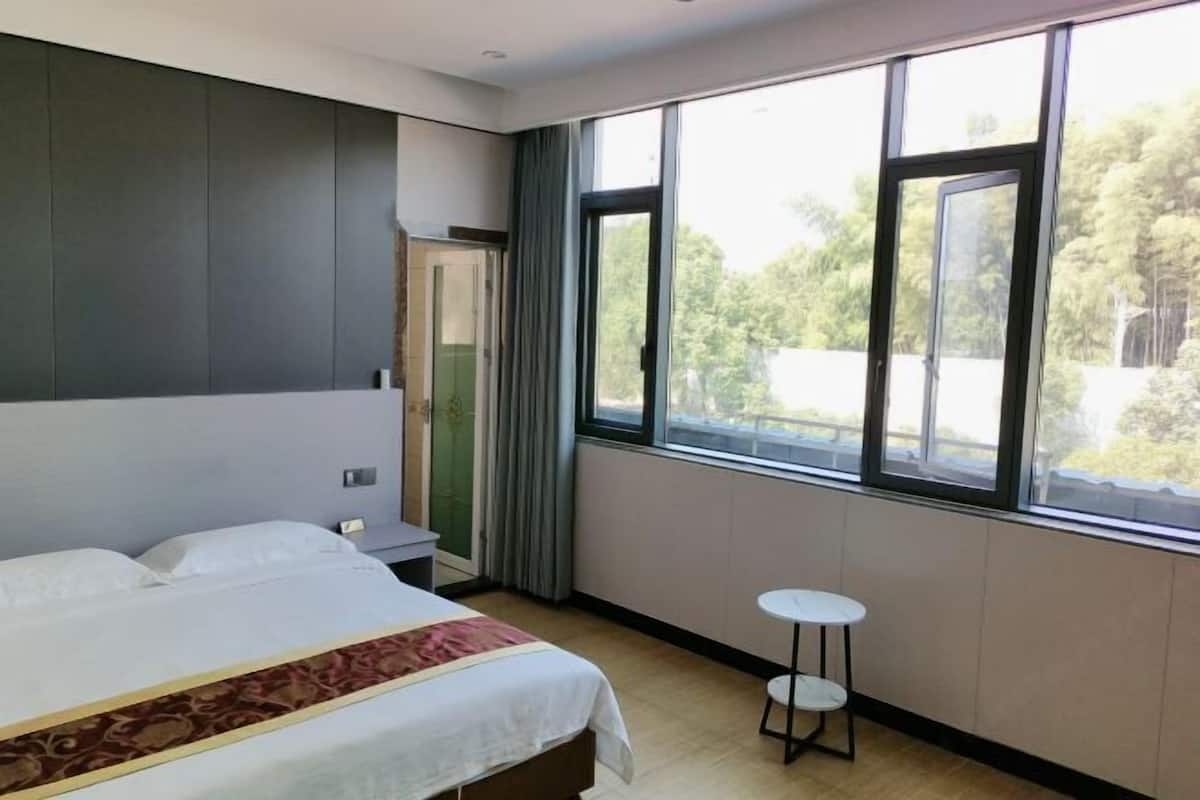 A hotel room with a large bed, a small table, and a window with a view of trees.