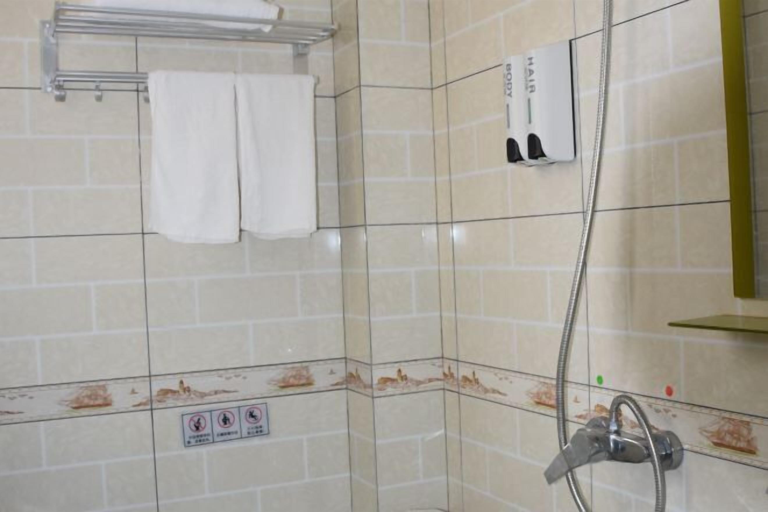 A bathroom with beige tiles, a towel rack, a shower head, and a soap dispenser.
