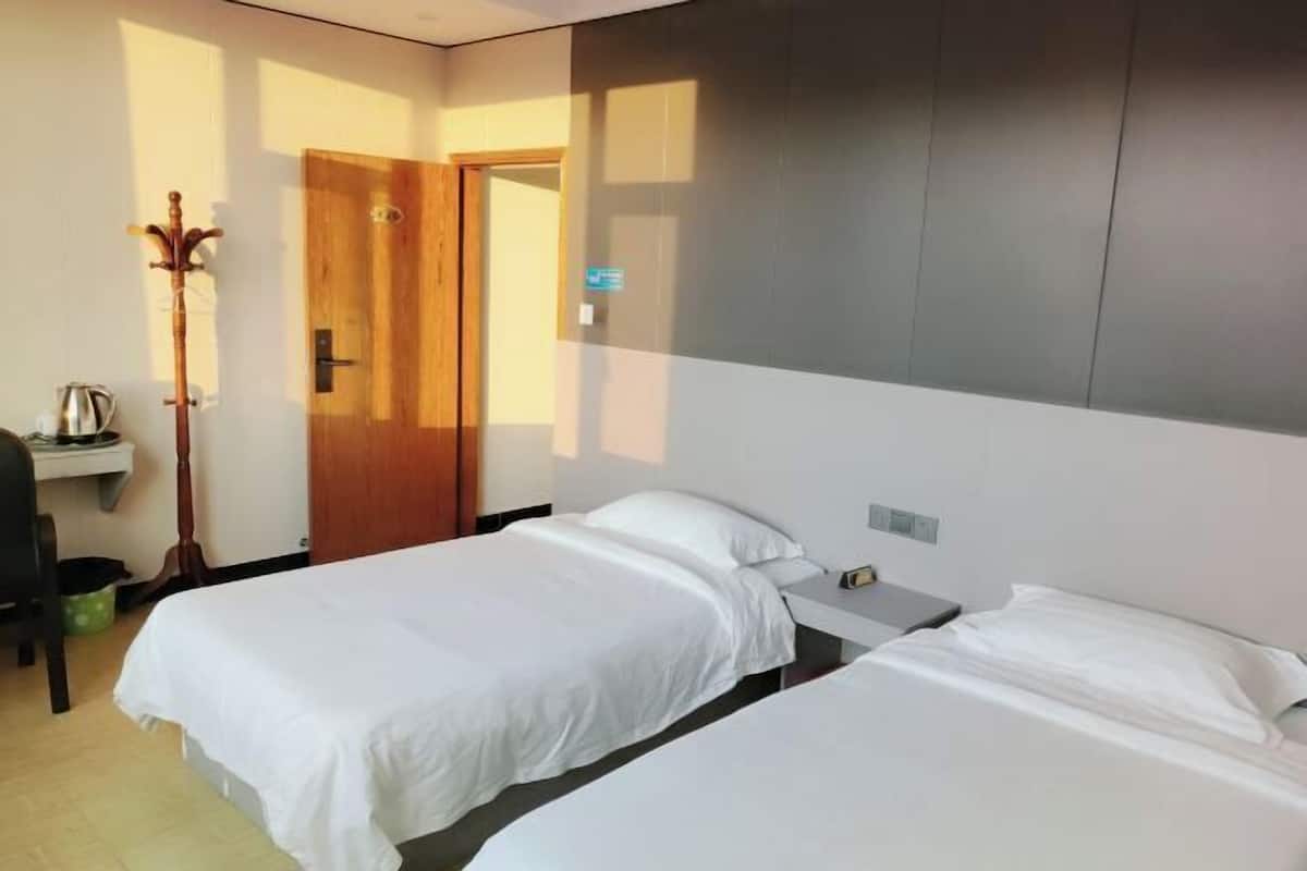 A hotel room with two beds, a desk, a chair, a coat rack, and a door.