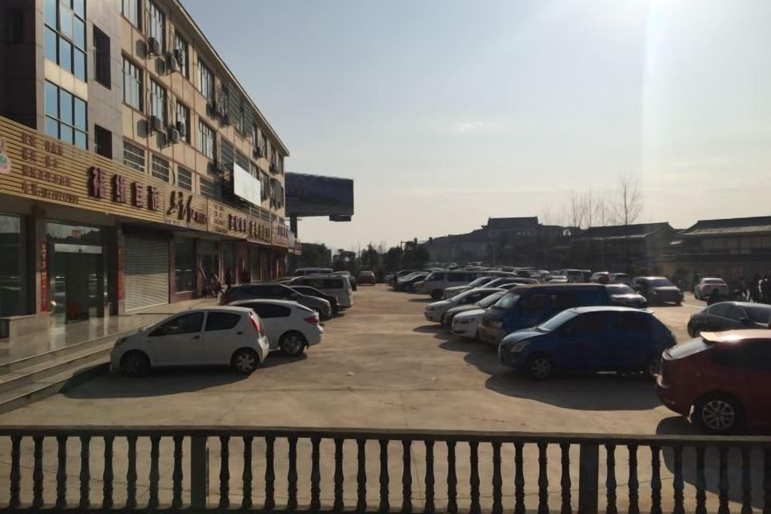 Un estacionamiento con varios autos y un edificio con comercios cerrados a la izquierda.