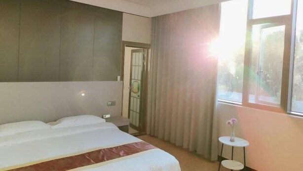 Une chambre d’hôtel avec un lit, une petite table sur laquelle se trouve un vase, et une fenêtre avec des rideaux.