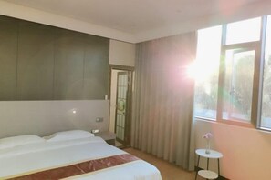 A hotel room with a bed, a small table with a vase, and a window with curtains. - Lushan Hanshe Homestay (Donglin Buddha) (Lushan City)
