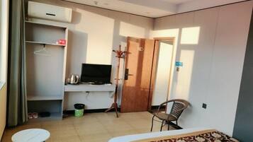 Habitación de hotel pequeña y funcional con cama, una mesita, una silla, televisor, armario y puerta.
