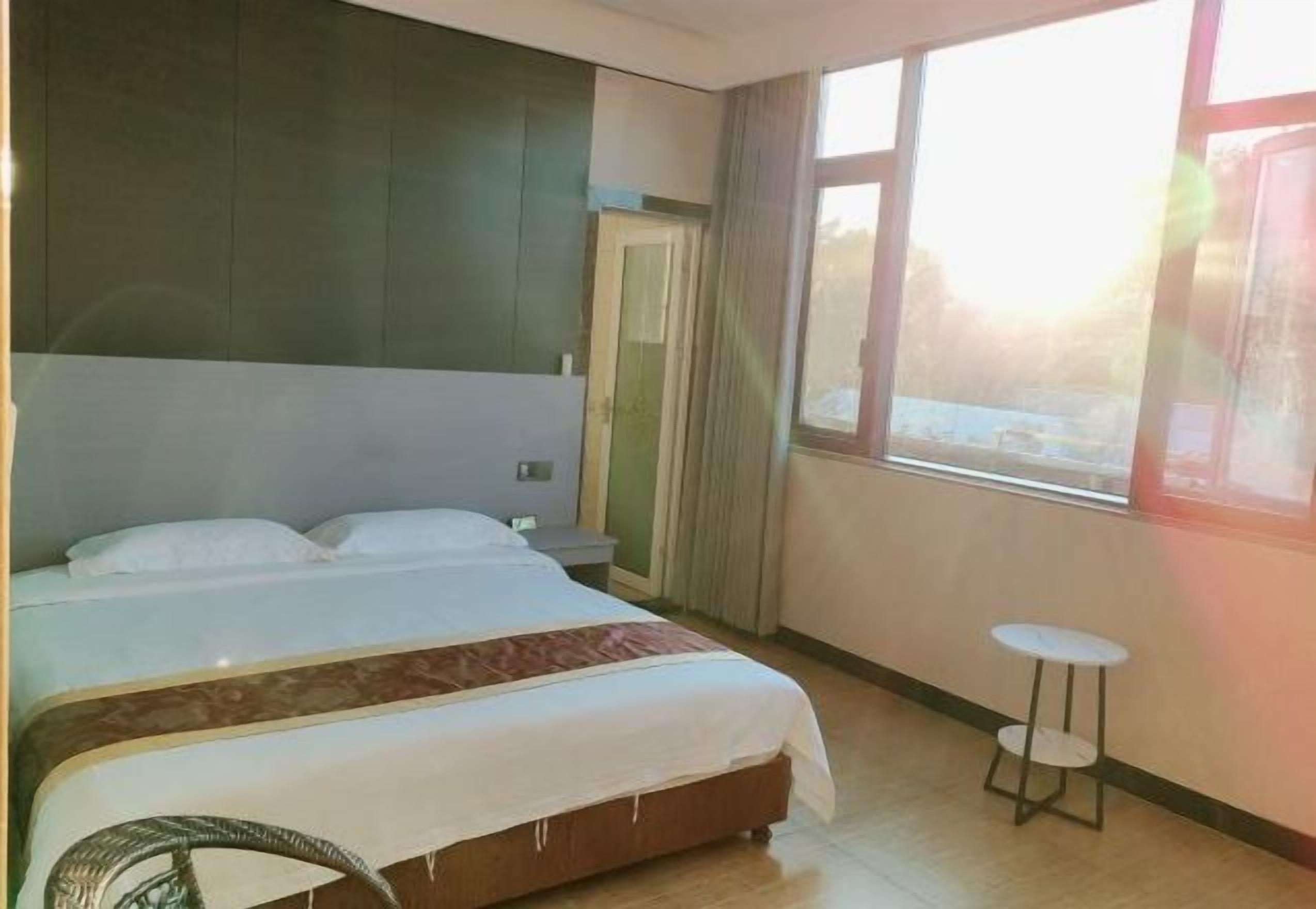 A hotel room with a bed, a small table, a window with a view, and a door.