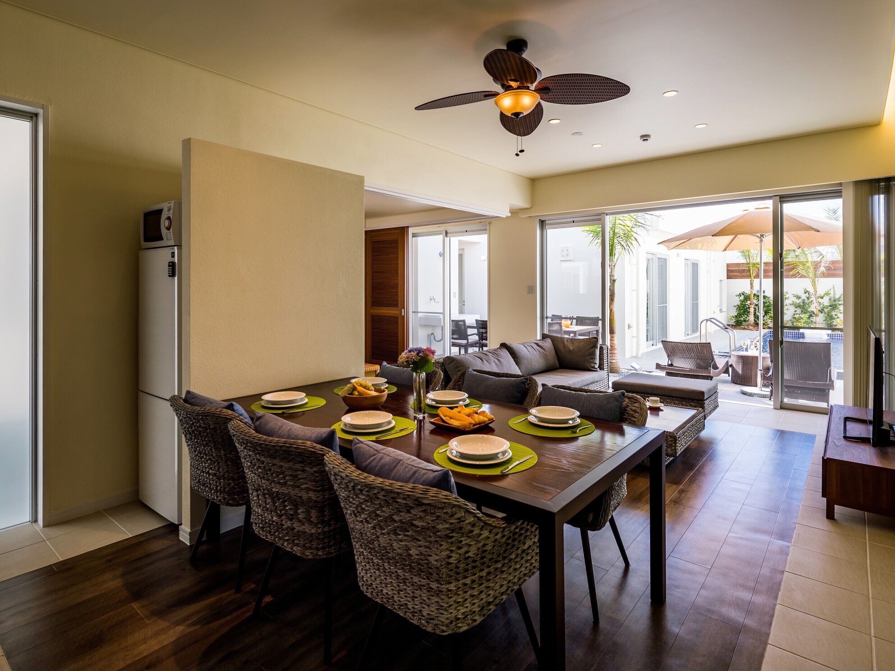 A dining area with a wooden table, wicker chairs, and a ceiling fan.