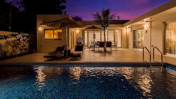 A modern outdoor pool area with lounge chairs and a dining table, surrounded by a covered patio and a glass-enclosed room.