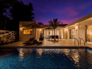 A modern outdoor pool area with lounge chairs and a dining table, surrounded by a covered patio and a glass-enclosed room. - Pool Villa Yagaji Island by Coldio Premium (Nago)