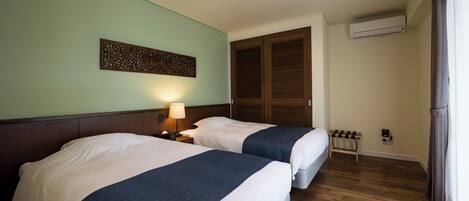 A hotel room with two beds, a nightstand with a lamp, a decorative wall piece, a wooden bench, and a window with curtains.