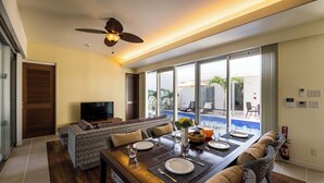 A dining area with a wooden table set for four, a sofa, and a television in the background.