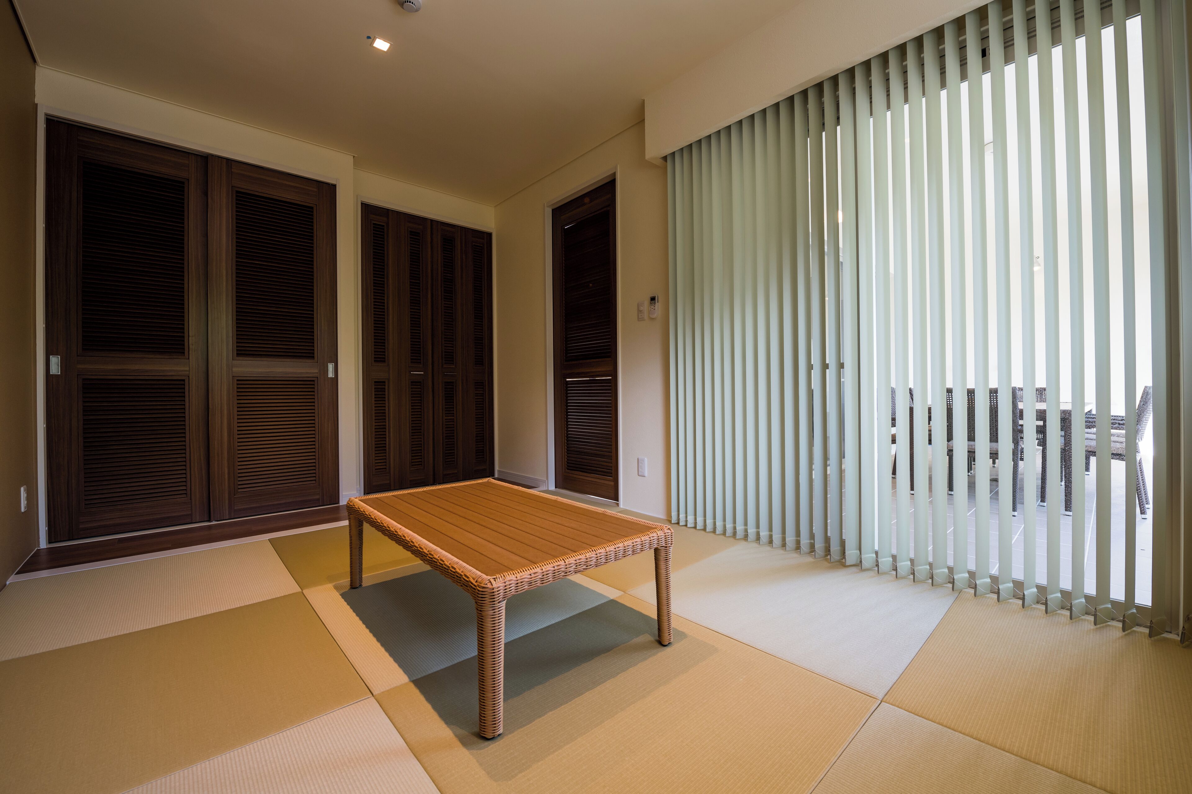 Een kamer met tatami matten, een houten tafel, schuifdeuren en uitzicht door verticale zonwering.