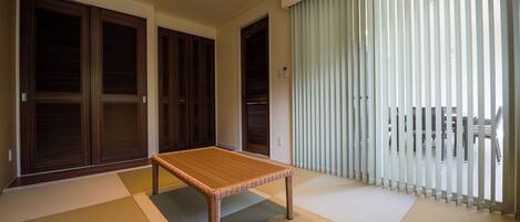 Habitación con esteras de tatami, una mesa de madera, puertas correderas y vistas a través de persianas verticales.