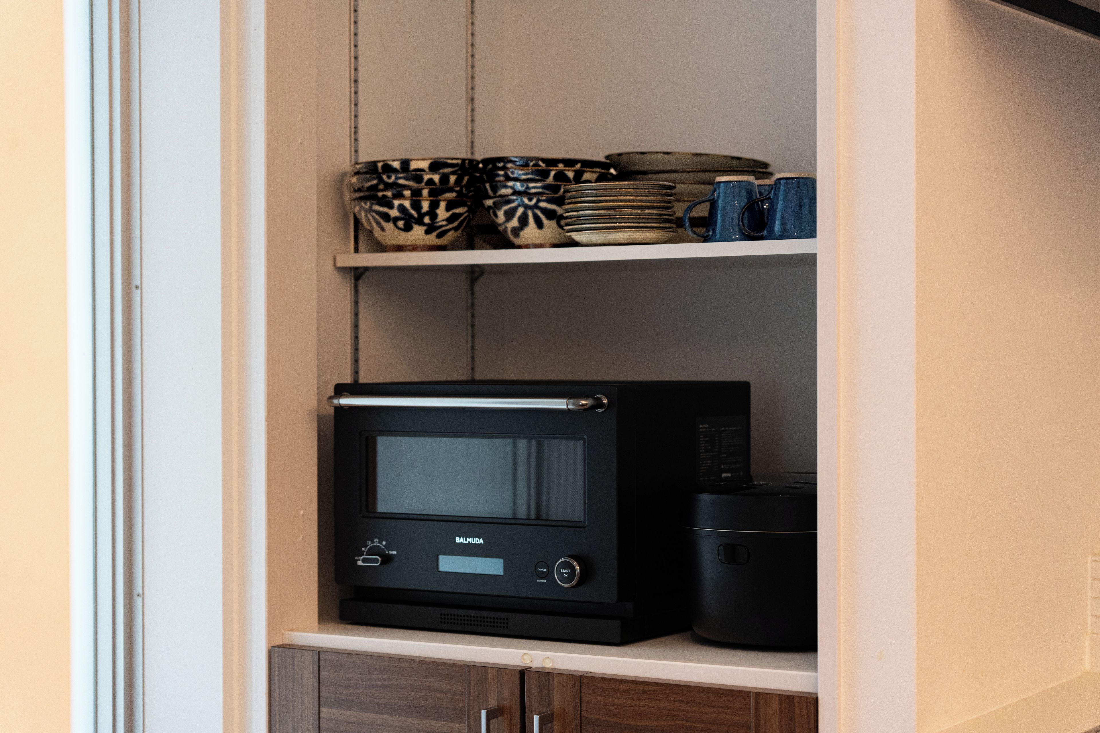 Een keuken met een magnetron, een koffiezetapparaat en gestapelde kommen op de plank.