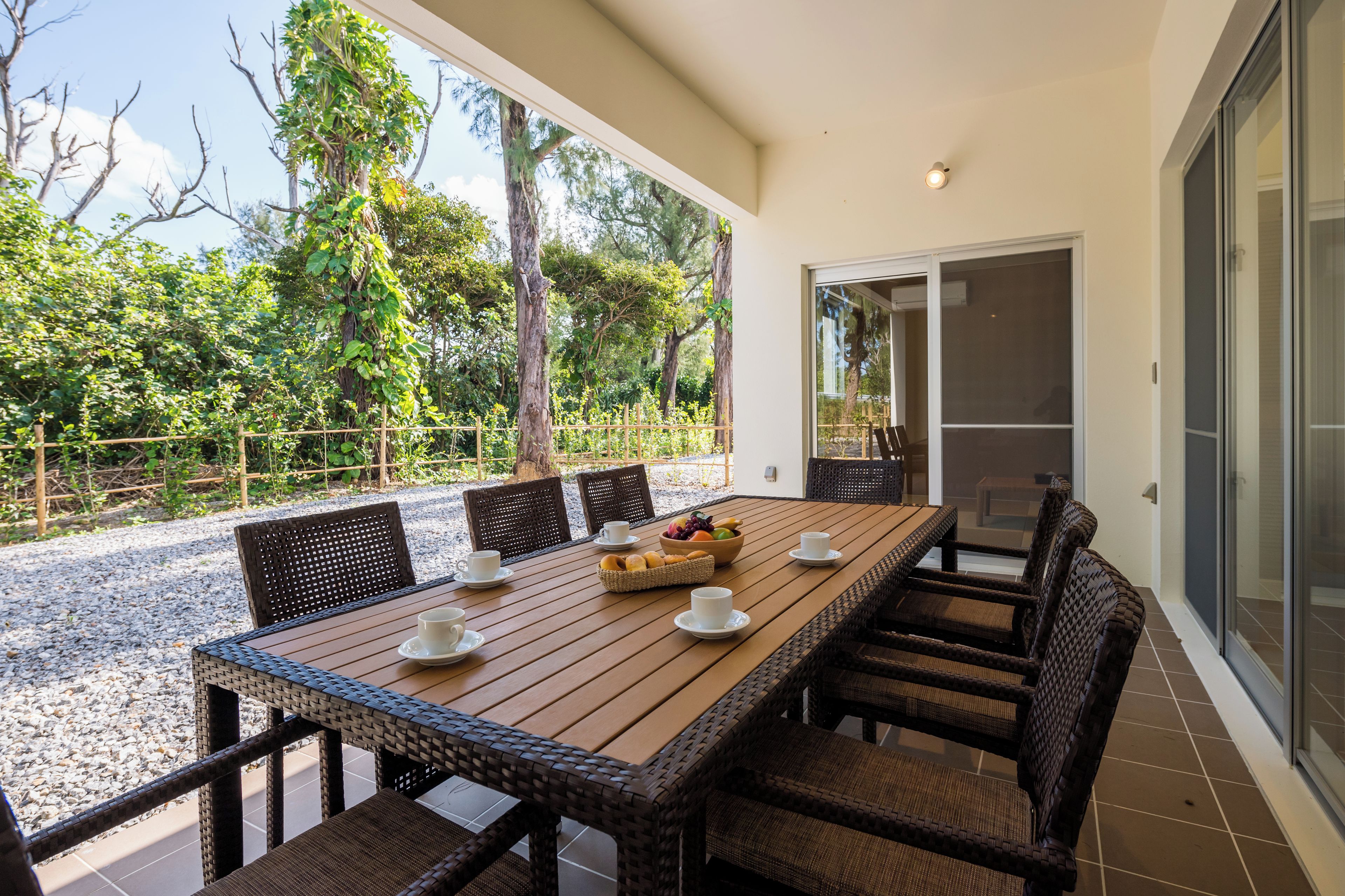 Un coin repas avec une longue table en bois, des chaises en osier et un saladier rempli de fruits.