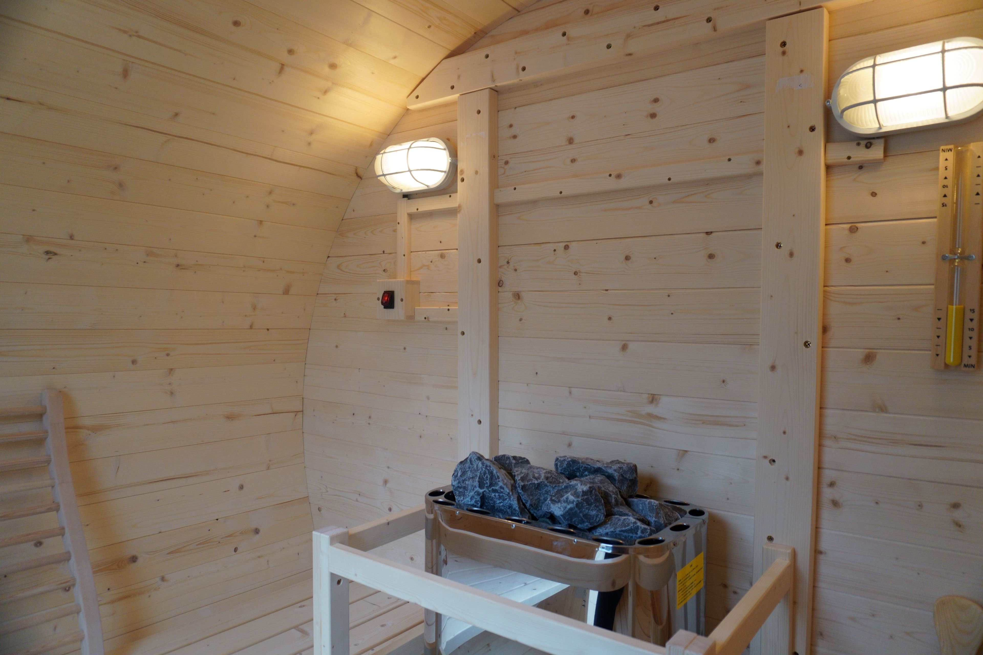 A wooden interior with a bench, a trash bin, and two wall-mounted light fixtures.