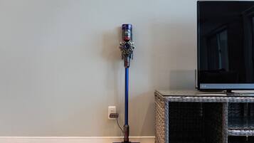 Un aspirateur Dyson est appuyé contre un mur, et à sa droite, sur un meuble, se trouve un téléviseur à écran plat.