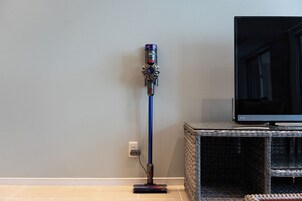 A Dyson vacuum cleaner standing upright against a wall with a flat-screen TV on a stand to the right.