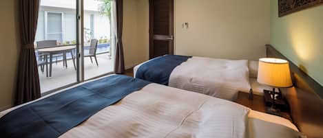 Una habitación de hotel con dos camas, una mesa con sillas, un balcón y una lámpara fijada a la pared.