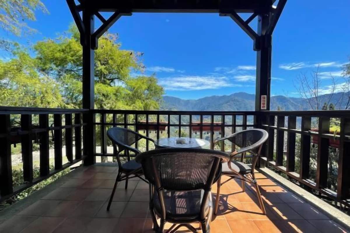 A covered outdoor seating area with a table and chairs, overlooking a mountainous landscape.