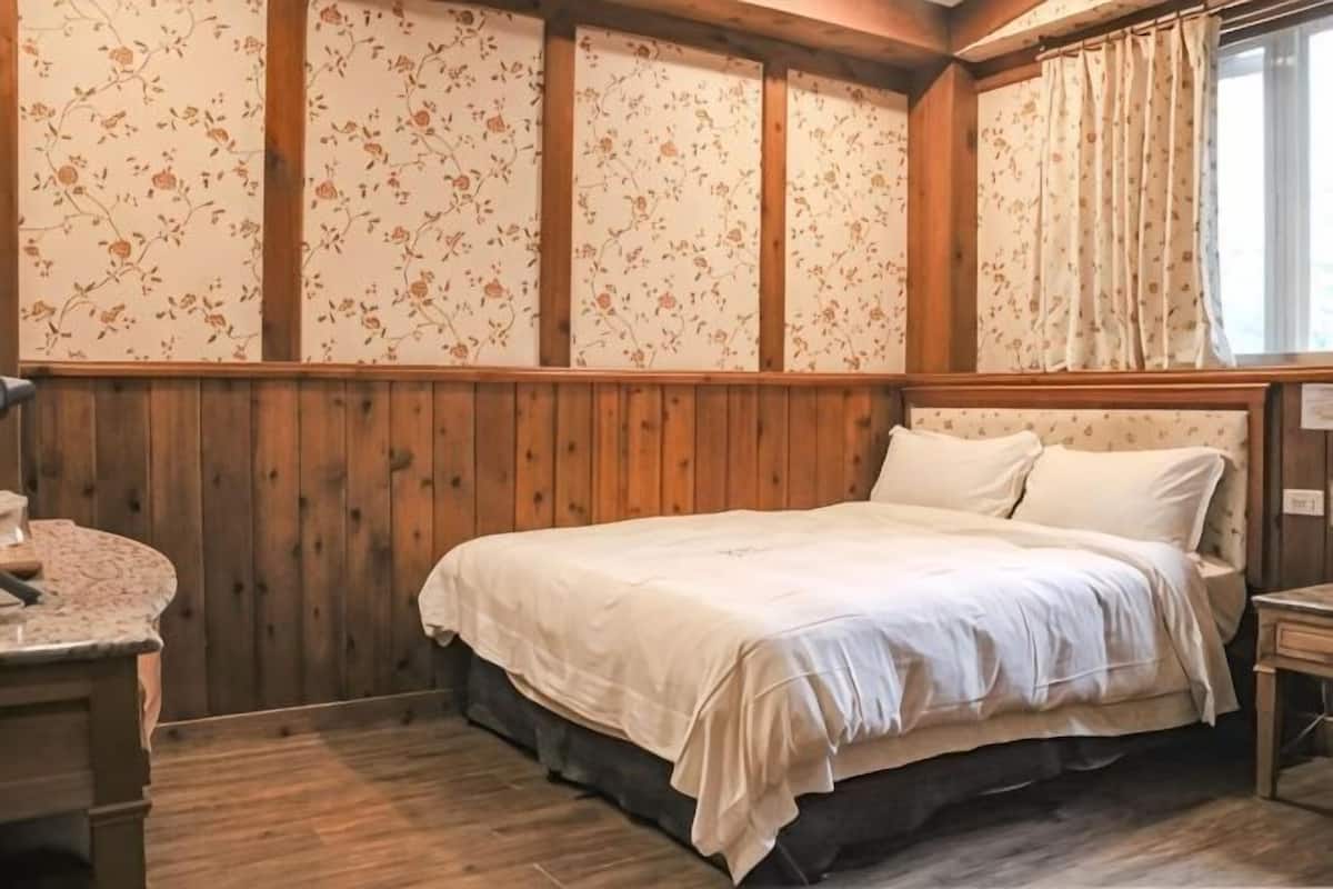 A bedroom with a wooden bed, floral wallpaper, and a window with curtains.