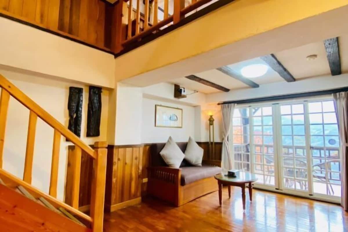 A wooden staircase, a sofa with cushions, a small table, and a large window with curtains.