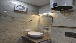 Ein Badezimmer mit Marmorwand, einem Waschbecken, einem Spiegel, einem Handtuchhalter und einer Deckenventilation.