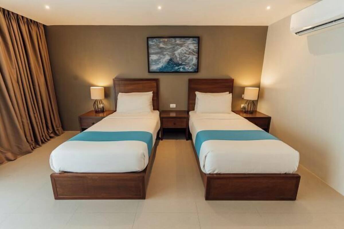 A hotel room with two beds, a large painting on the wall, and an air conditioning unit.