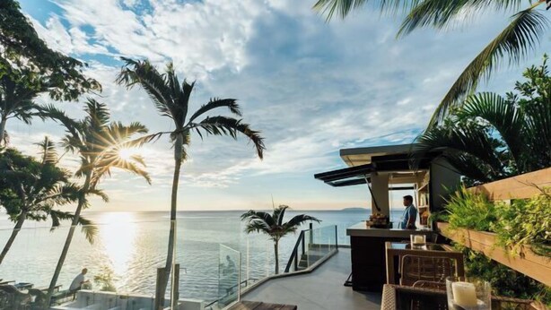 Eine Terrasse mit Blick auf das Meer, Palmen und ein Holzdeck.