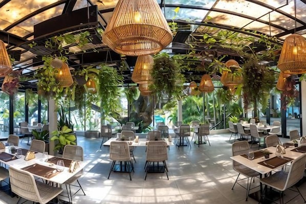 A restaurant with tables and chairs, hanging wicker lamps, and greenery.