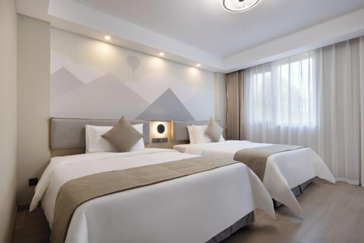 Une chambre d’hôtel avec deux lits, une lampe fixée au mur et une fenêtre avec des rideaux.