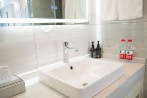 Un lavabo blanc dans la salle de bain, avec un robinet chromé, un miroir au-dessus et deux flacons de savon pour les mains posés sur le comptoir.