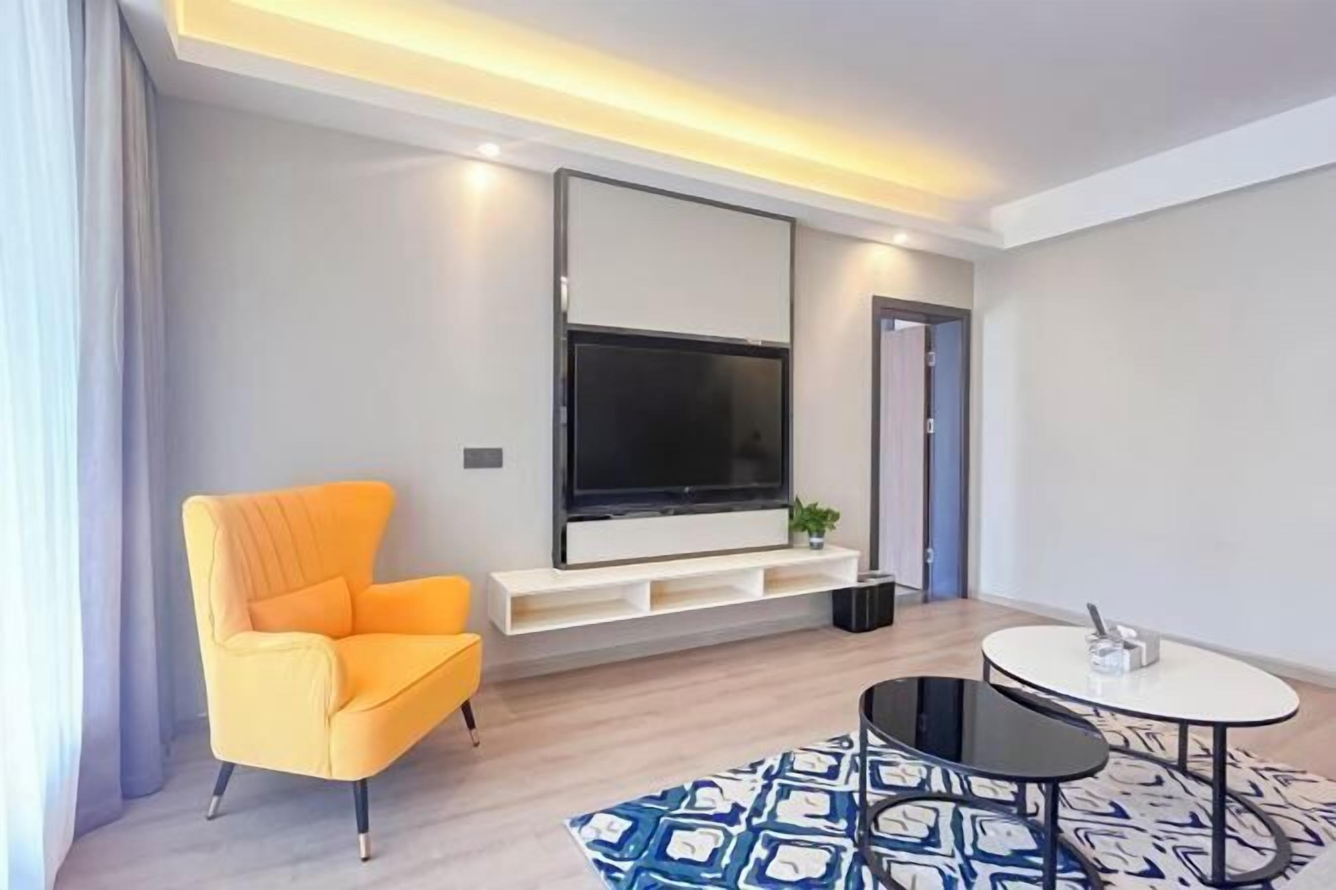 Una sala de estar moderna con un televisor de pantalla plana grande, un sillón naranja brillante, una mesita redonda y una alfombra estampada.