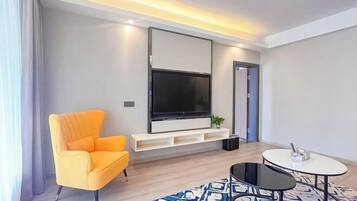 Una sala de estar moderna con un televisor de pantalla plana grande, un sillón naranja brillante, una mesita redonda y una alfombra estampada.