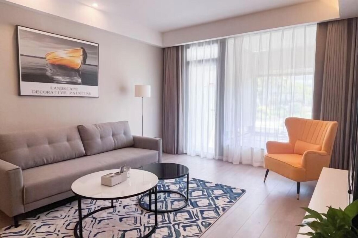 Un salon moderne avec un canapé, une table basse ronde, un fauteuil et une grande fenêtre avec des rideaux.