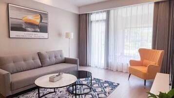 Una sala de estar moderna con un sofá, una mesa redonda de centro, una silla y un ventanal con cortinas.
