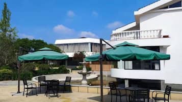 An outdoor patio with tables and chairs, umbrellas, and a fountain.