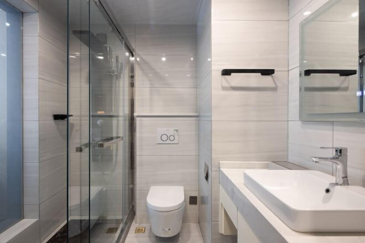 Une salle de bain moderne avec une douche à parois de verre, des toilettes blanches et un grand lavabo surmonté d’un miroir.