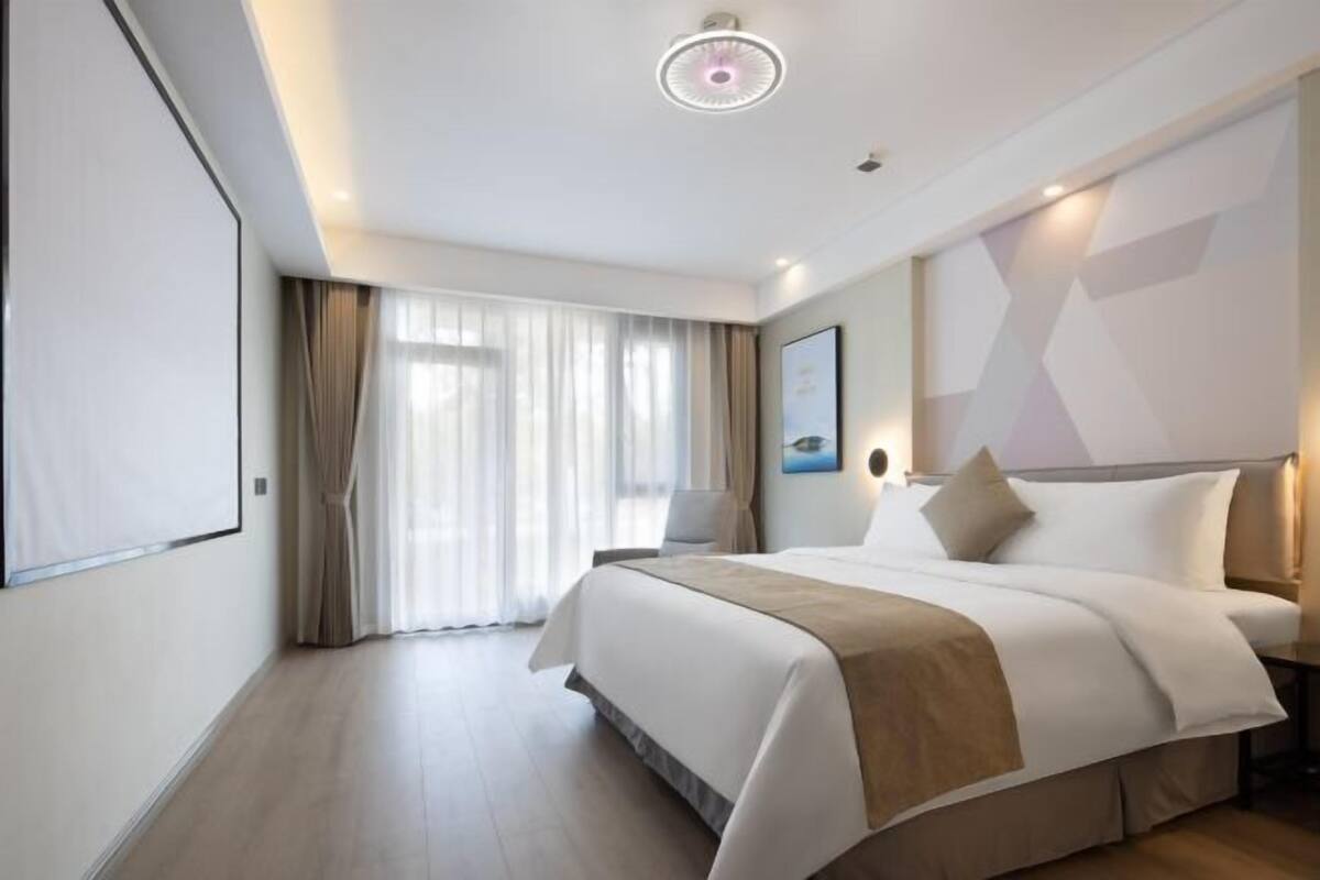 Ein modernes Hotelzimmer mit einem großen Bett, einem Nachttisch, einem Wandbild und einer Deckenleuchte.