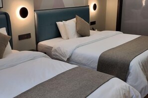 Hotellihuone, jossa on kaksi sänkyä. Jokaisessa sängyssä on pääty, valkoiset vuodevaatteet ja harmaa torkkupeitto.