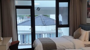 Ein Hotelzimmer mit Bett, Schreibtisch und Blick auf einen Balkon mit Ziegeldach.