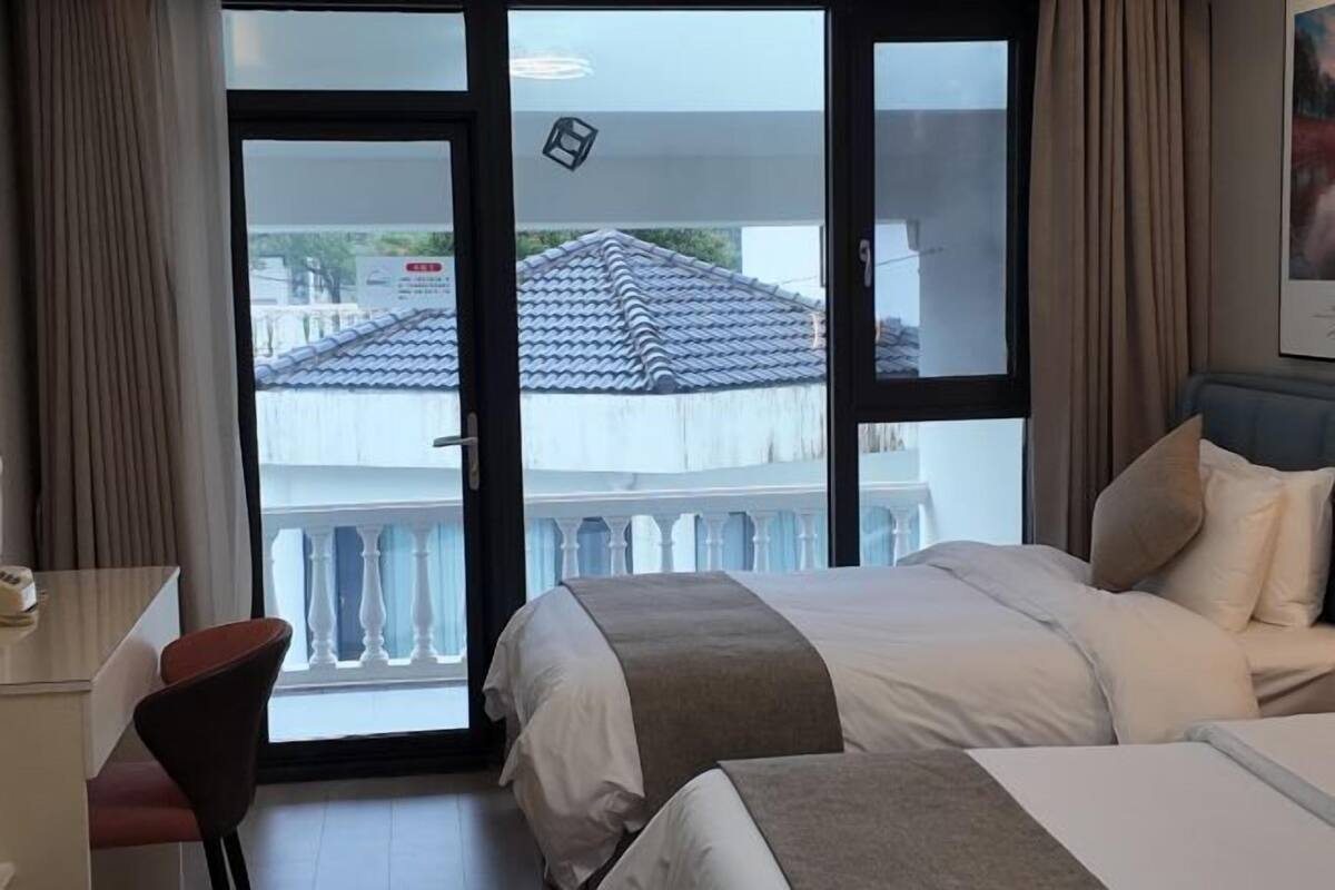 Ein Hotelzimmer mit Bett, Schreibtisch und Blick auf einen Balkon mit Ziegeldach.