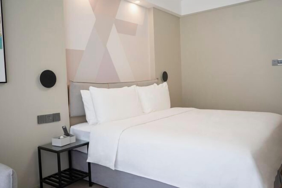 Une chambre d’hôtel moderne avec un lit soigneusement fait, une table de chevet avec une lampe et un luminaire fixé au mur.