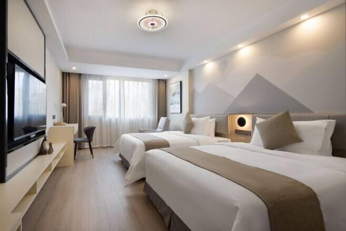 Ein Hotelzimmer mit zwei Betten, einem Fernseher, einem Schreibtisch und einem Fenster mit Vorhängen.