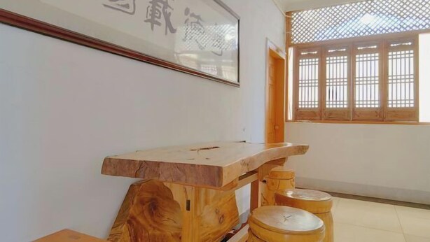 A room with a wooden table, stools, a framed sign, and a window with a lattice design.