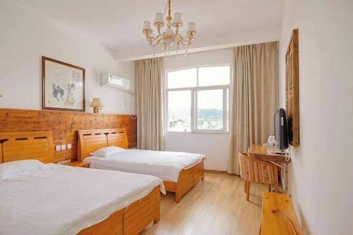 A hotel room with two beds, a wooden headboard, a television, a desk, and a window with a view.