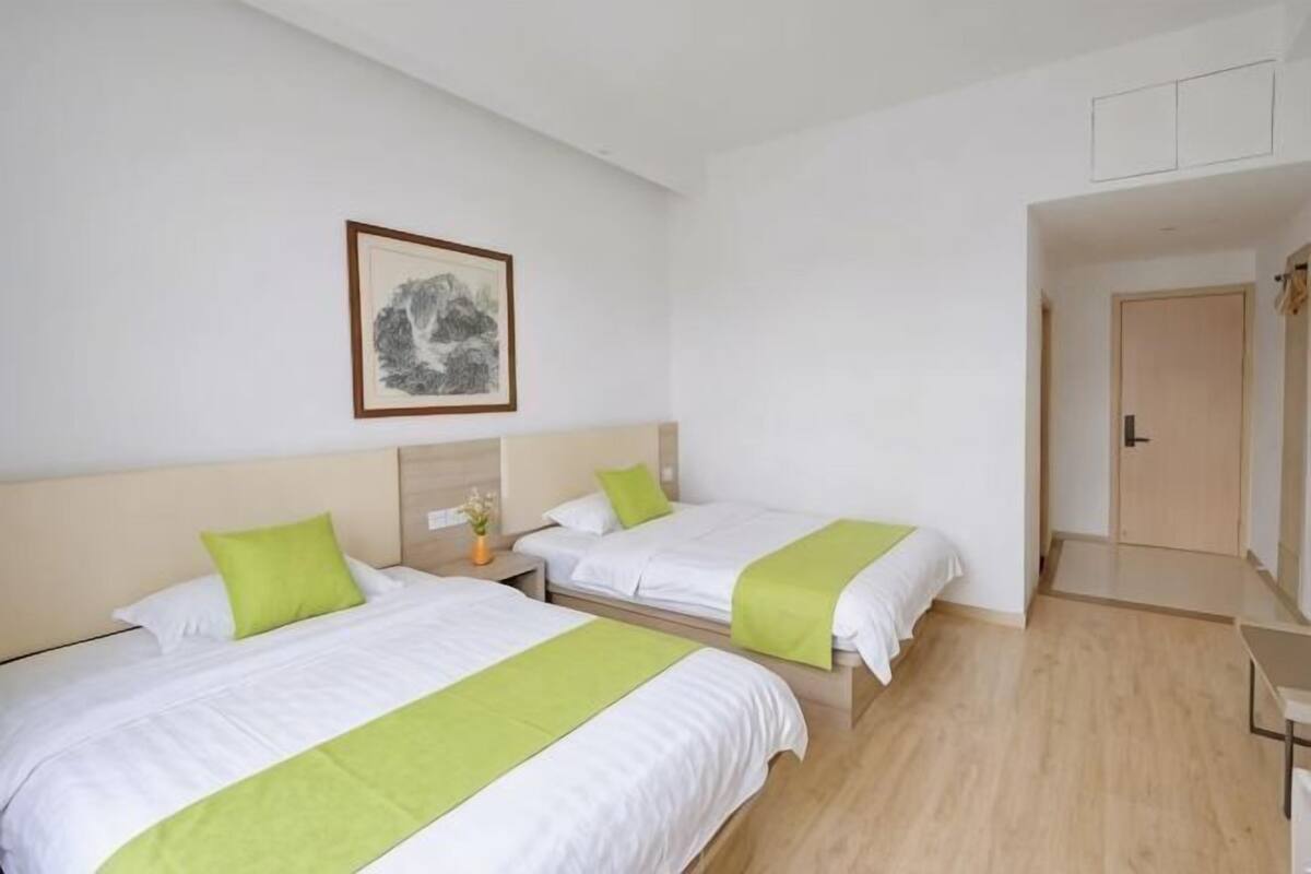 A hotel room with two beds, a nightstand, a framed picture on the wall, and a door leading to another room.