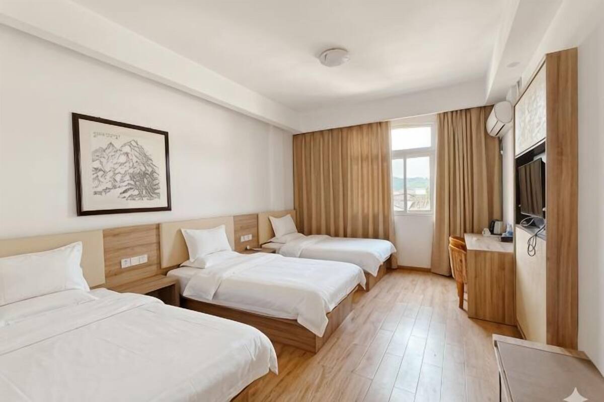 A hotel room with three beds, a desk, a chair, a TV, and a window with curtains.
